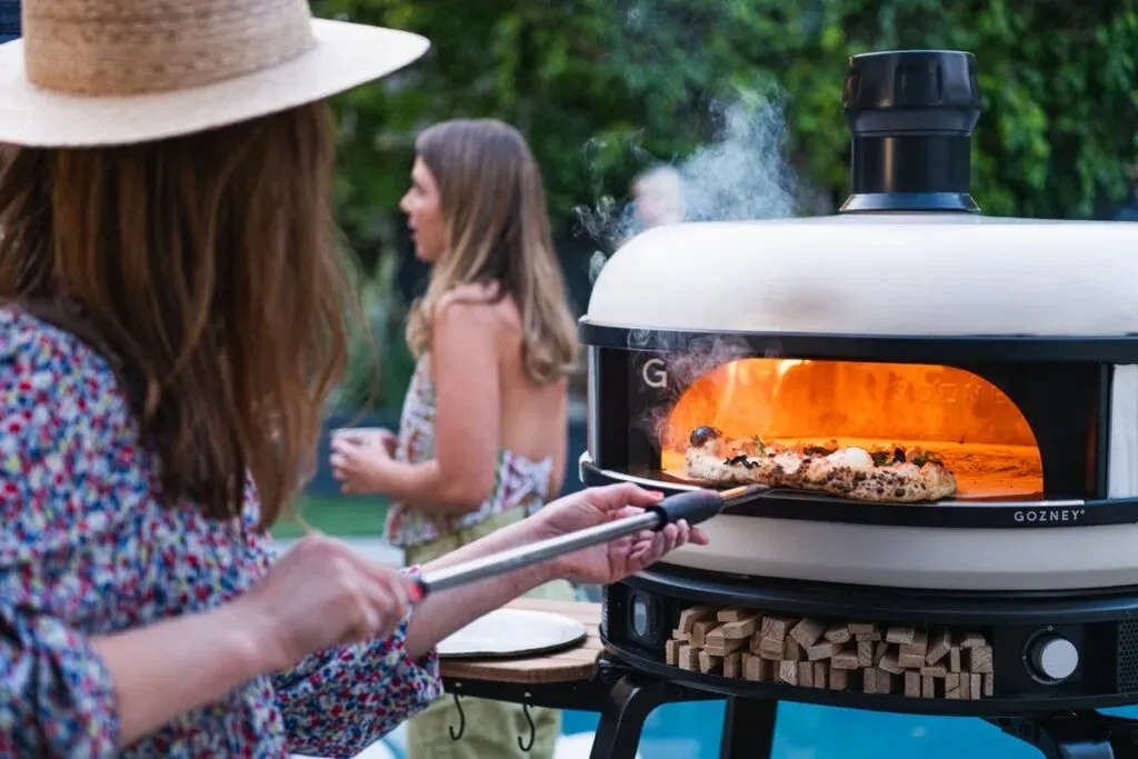 Gozney Dome pizza oven with a woman grilling a pizza